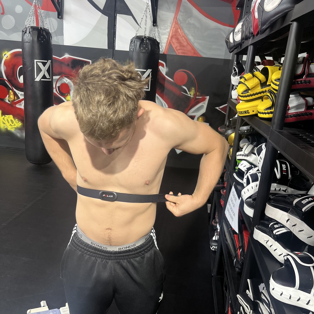 Krane fitting a Polar heart rate strap in the gym, punching bags behind him.