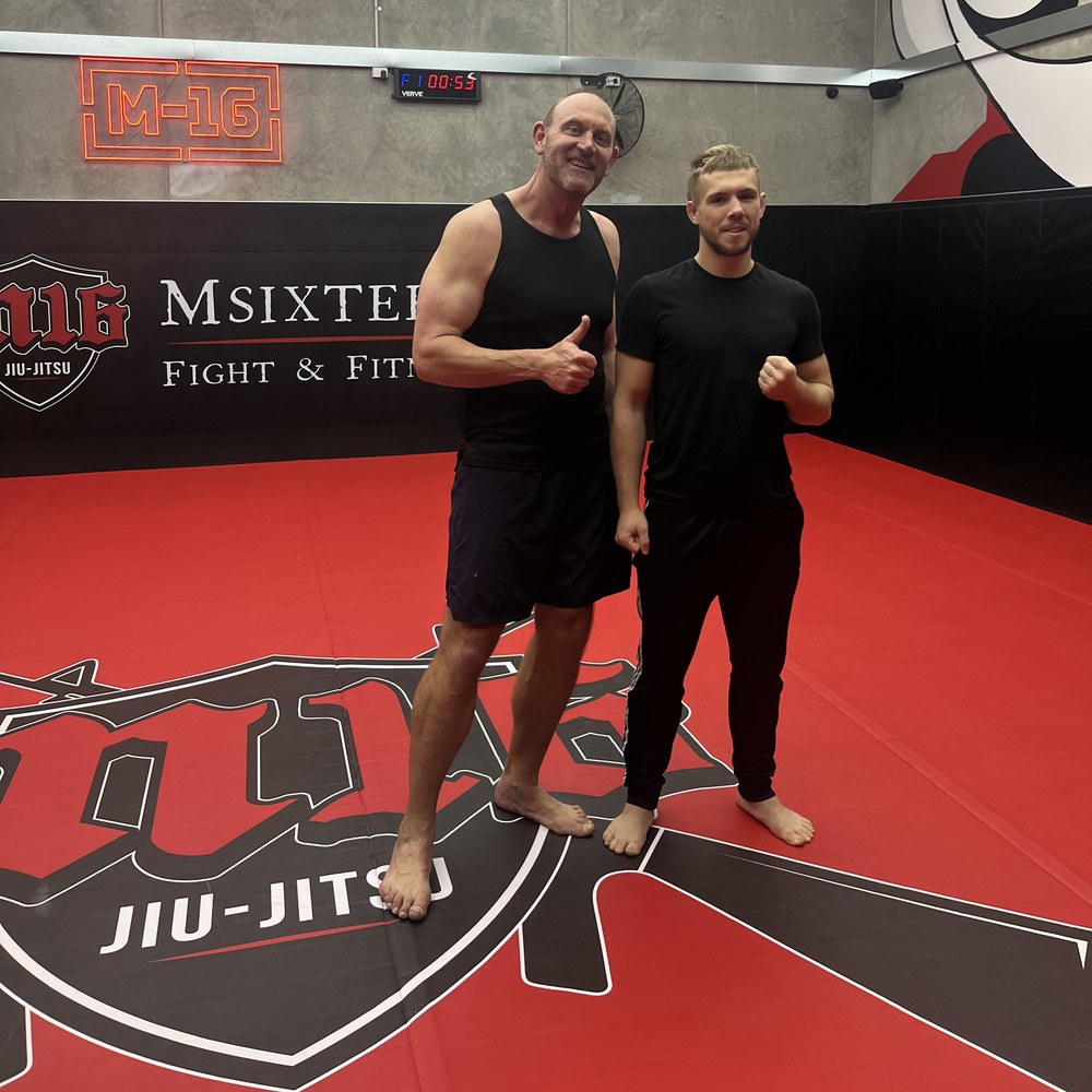 Krane on the mats at M16, in front of the gym's wall branding.